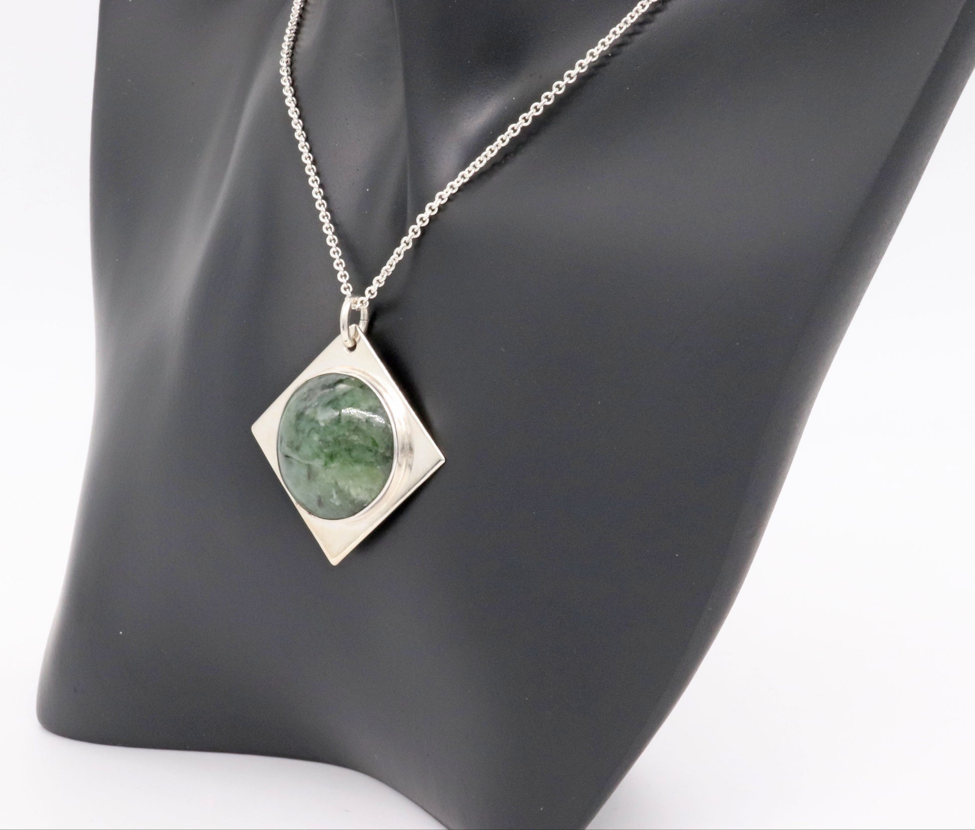 Wyoming Jade cabochon stone set in solid Argentium silver paired with Argentium silver 1.7 chain. Shown on black resin jewelry form against white background.