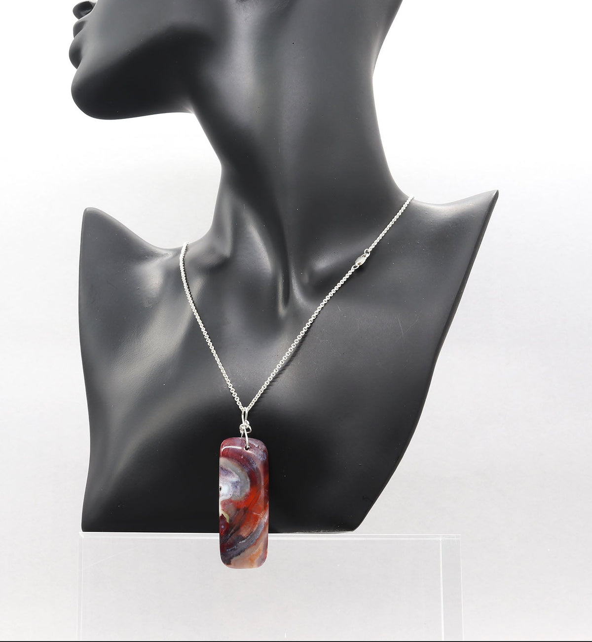 An Argentium silver chain necklace with a rectangular banded agate pendant featuring a red, orange, and white marbled pattern, displayed on a black mannequin bust against a white background.
