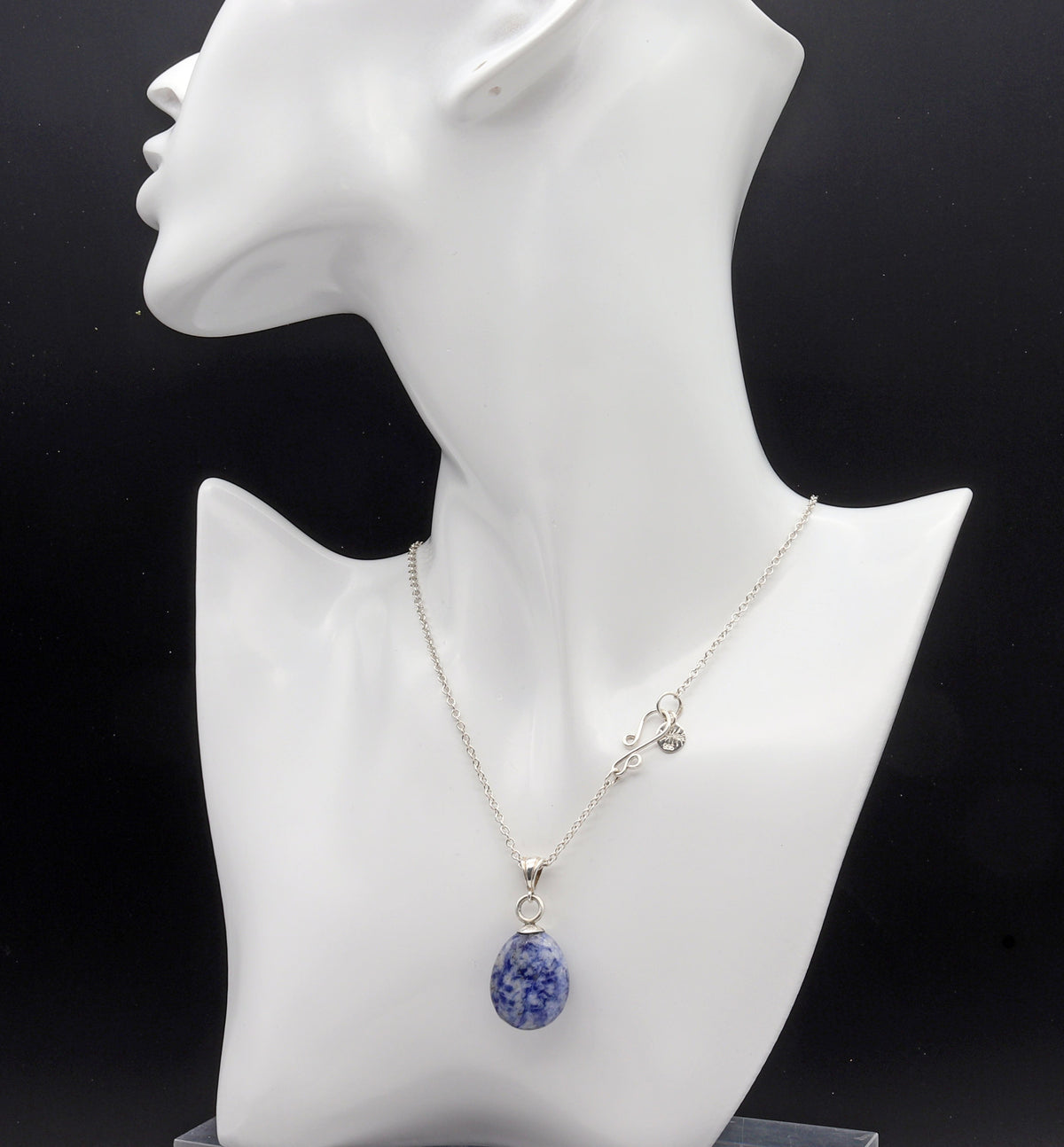 One-of-a-kind Blue Sodalite teardrop pendant, hand-cut and polished in our Missouri studio shown on white resin jewelry form on black background.  Paired with Argentium Silver necklace with s-hook clasp.