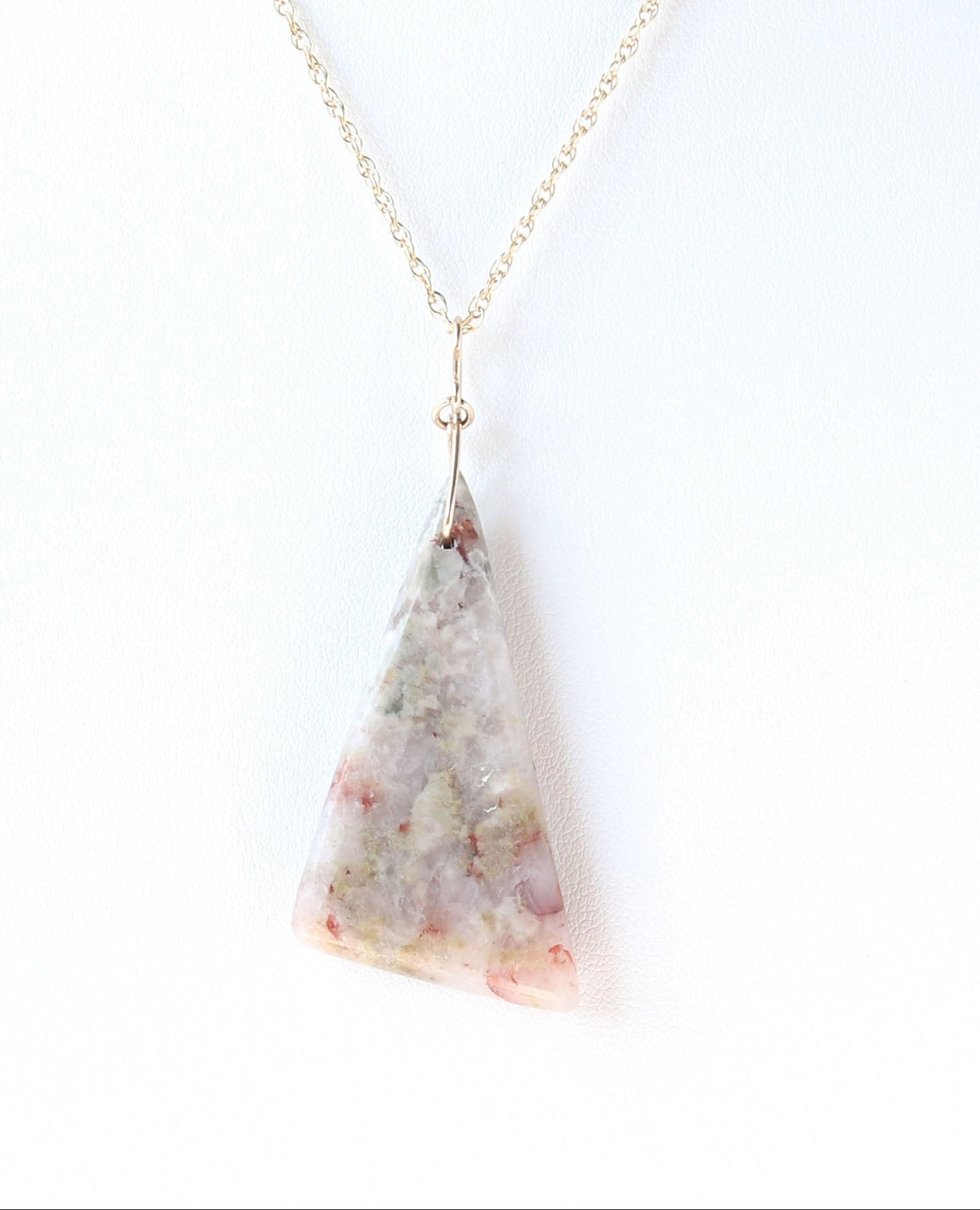 A Sunstone pendant, hand-cut and polished on both sides to showcase the natural blend of reds, muted greens and softly translucent areas of the stone. The irregular triangular shape is finished with a handcrafted 14/20 gold-filled infinity bow-style bail.