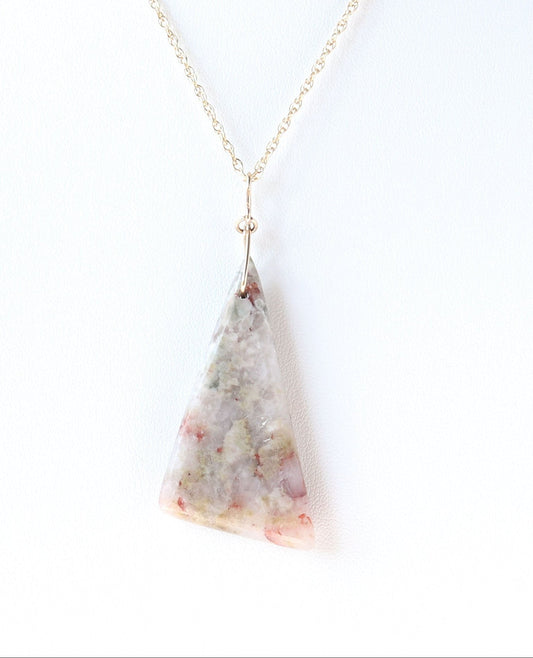 A Sunstone pendant, hand-cut and polished on both sides to showcase the natural blend of reds, muted greens and softly translucent areas of the stone. The irregular triangular shape is finished with a handcrafted 14/20 gold-filled infinity bow-style bail.