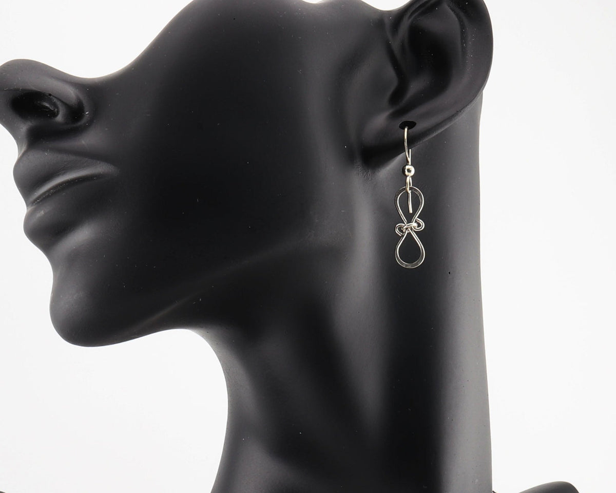 Infinity bow earrings shown on black resin jewelry modeling against white background.  