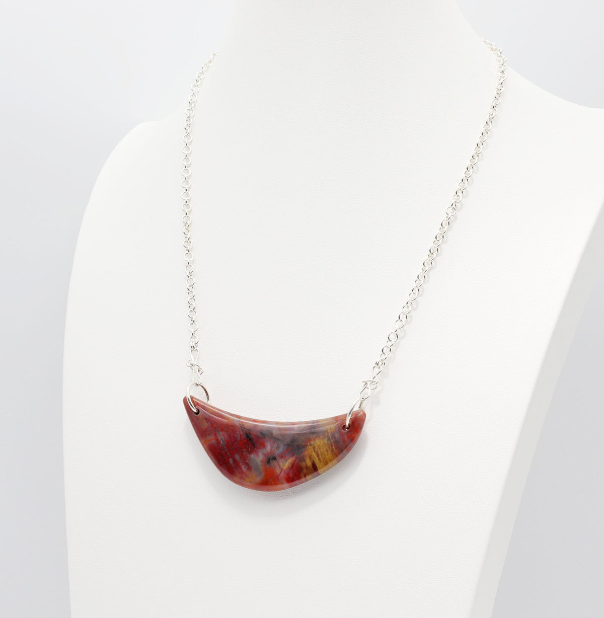 Necklace with attached crescent shaped Petrified Rainbow Wood pendant is shown on white jewelry mannequin model for length and styling inspiration.  Shown against a white background.