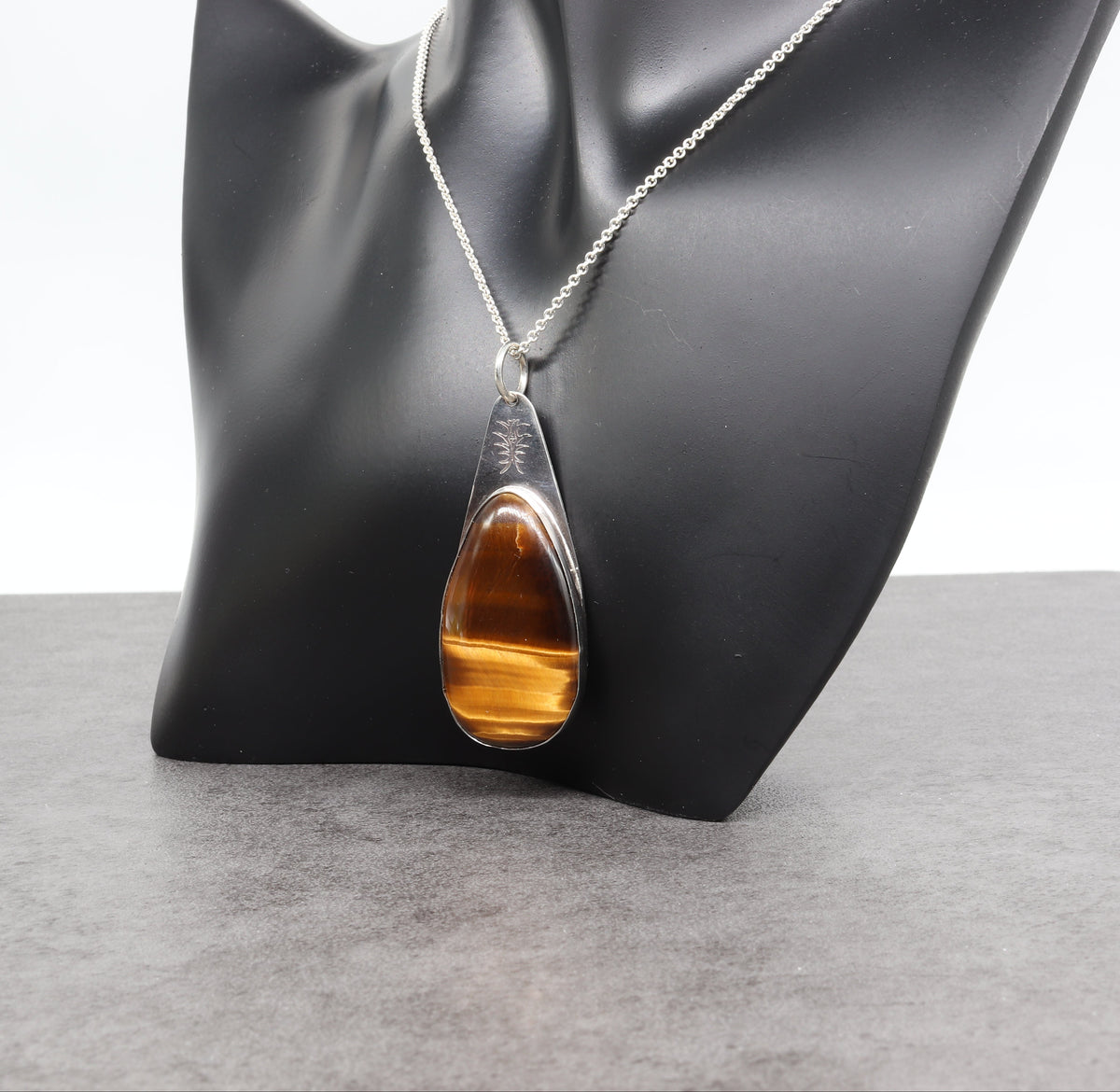 Tigers eye teardrop pendant necklace in Argentium silver  displayed on a black jewelry bust against a light gray background.