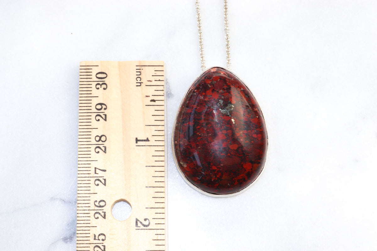 Red Brecciated Jasper next to wood ruler to illustrate size shown on white marble background.
