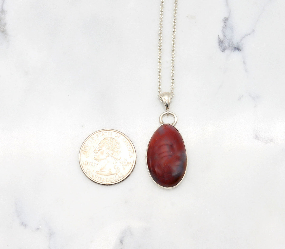 Arizona Petrified Rainbow Wood pendant, laid flat next to a U.S. quarter for size perspective on white marble background.