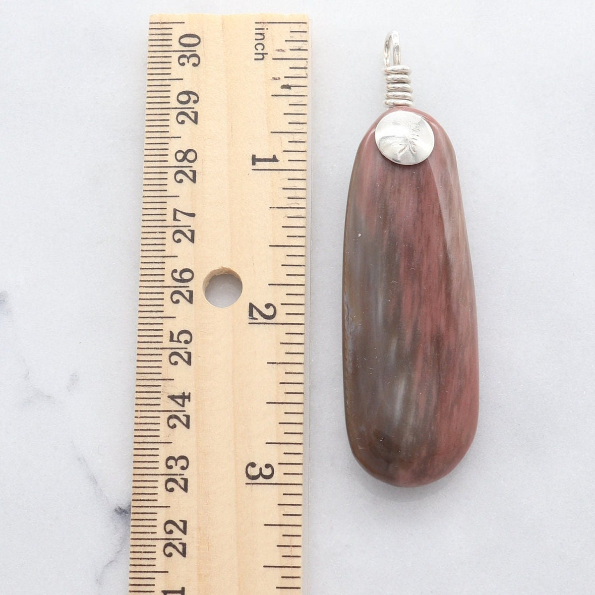 Arizona Petrified Rainbow Wood pendant beside ruler showing approximately 3 inch overall length.  Shown against white marble slab.