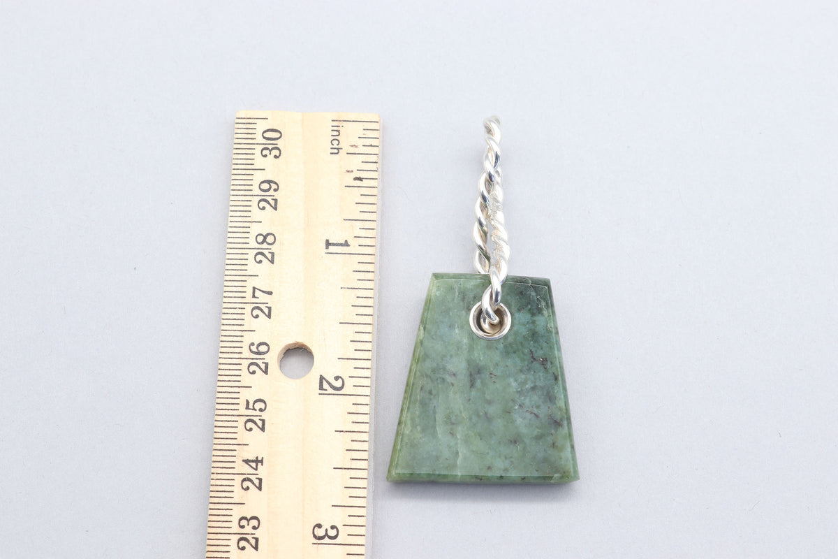 A green Wyoming jade stone pendant with a twisted silver bail and chain, shown next to a wooden ruler for scale on a light gray background.
