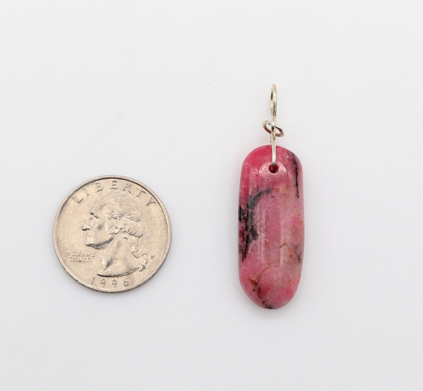 This 1.79 inch Pendant is. shown next to quarter for scale. natural pink Rhodonite crystal pendant with black inclusions, handcut and polished to showcase its natural beauty on either side. crafted with a custom infinity bow shaped bail, in Argentium 935 silver shown on white background.