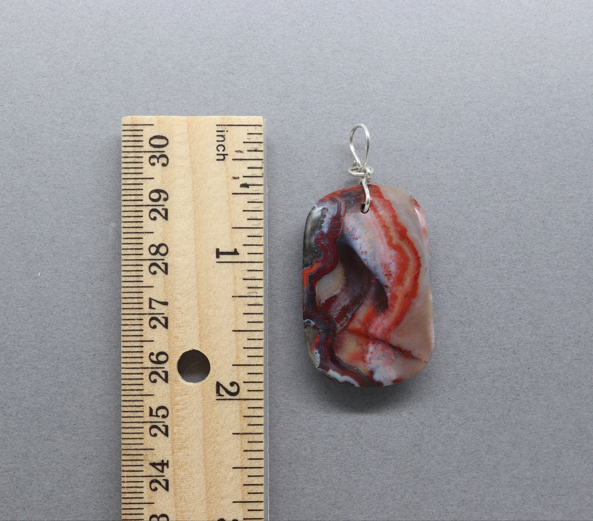 Red Mexican Banded Agate shown next to  a wooden ruler for scale on a gray background.