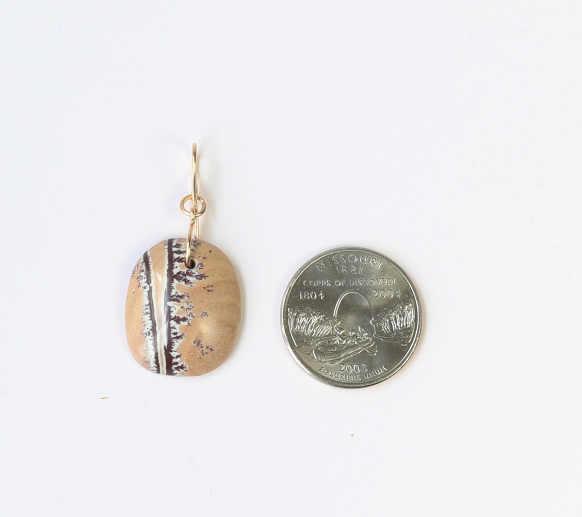 A small natural Sonoran dendrite rhyolite pendant with a gold fill wire bail. The pendant is shown next to a Missouri state quarter to illustrate scale of size.  Shown on white background.