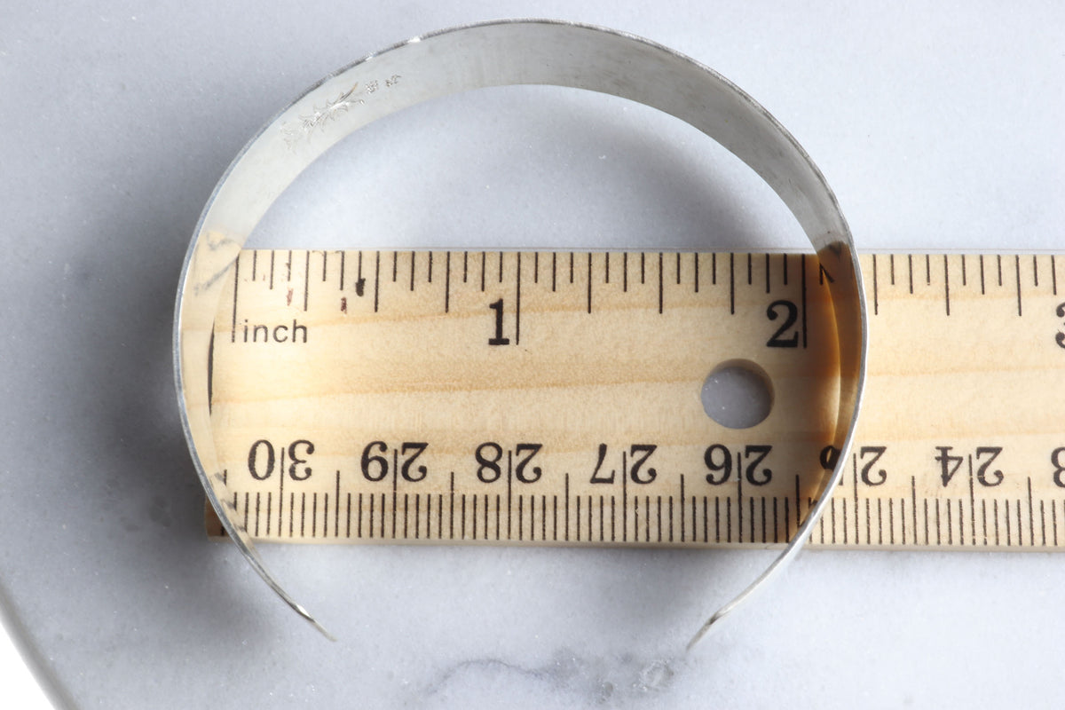 Hand-hammered Argentium 935 silver cuff bracelet shown with a wooden ruler measuring the approximately 1/2 inch band width on a light gray marble surface.