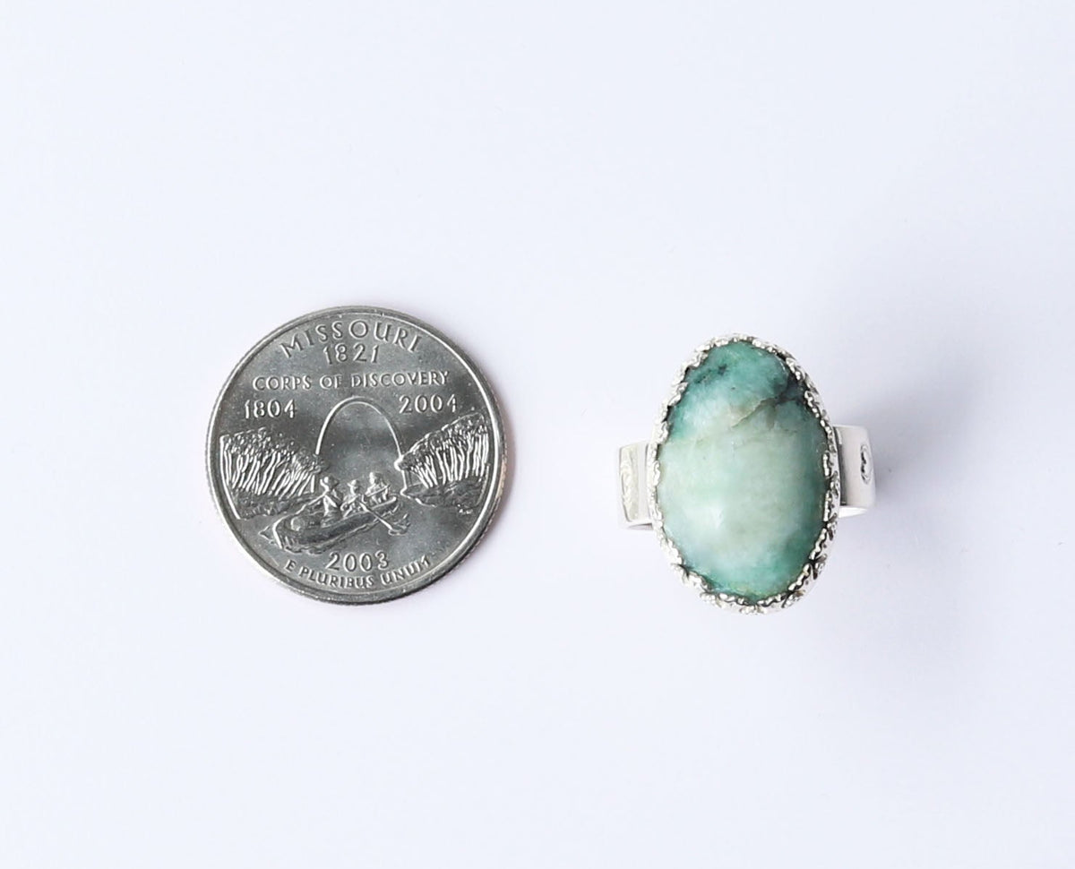 A silver ring with an oval green stone, shown next to a US quarter for scale on a plain white background.