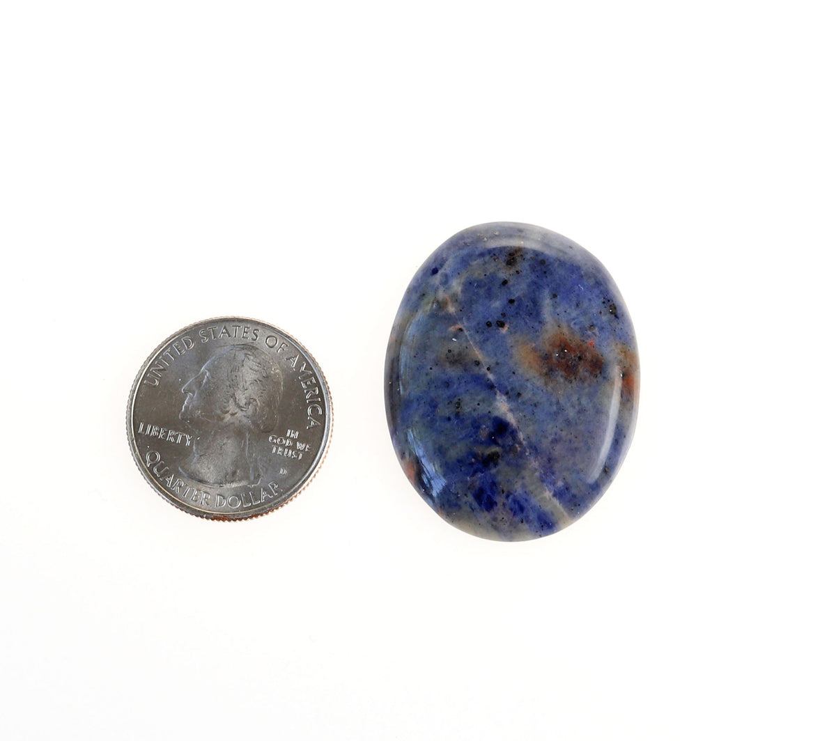 Hand-cut Blue Foidolite Sodalite oval cabochon with mottled blue, creamy white, gray, and warm brown natural patterns.  Shown next to a U.S. quarter for scale against a white background.