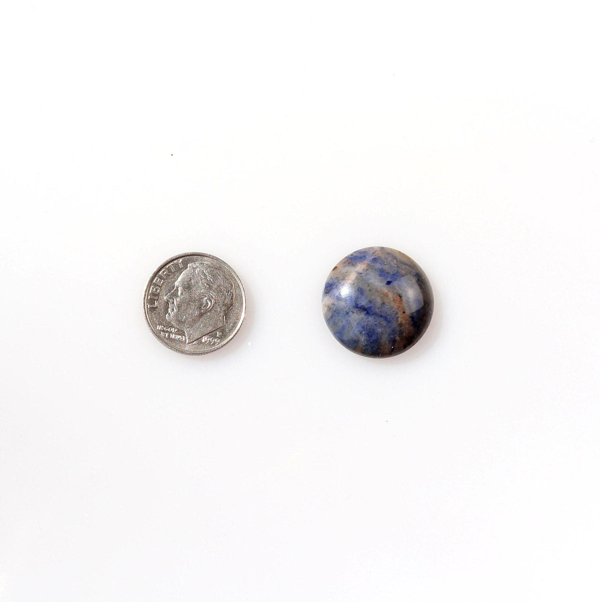 A single round Blue Foidolite Sodalite cabochon hand-cut 19.64 mm with a marbled pattern of deep blue, slate gray, and brown, next to a U.S. dime and photographed on a clean white background.