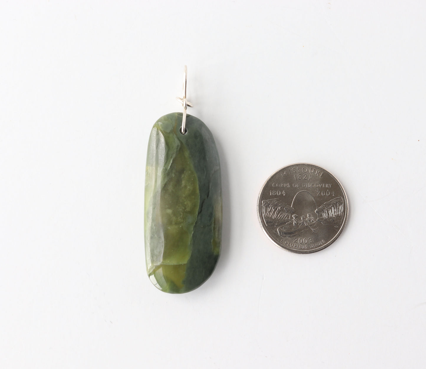 Green jade pendant next to a quarter on a white background