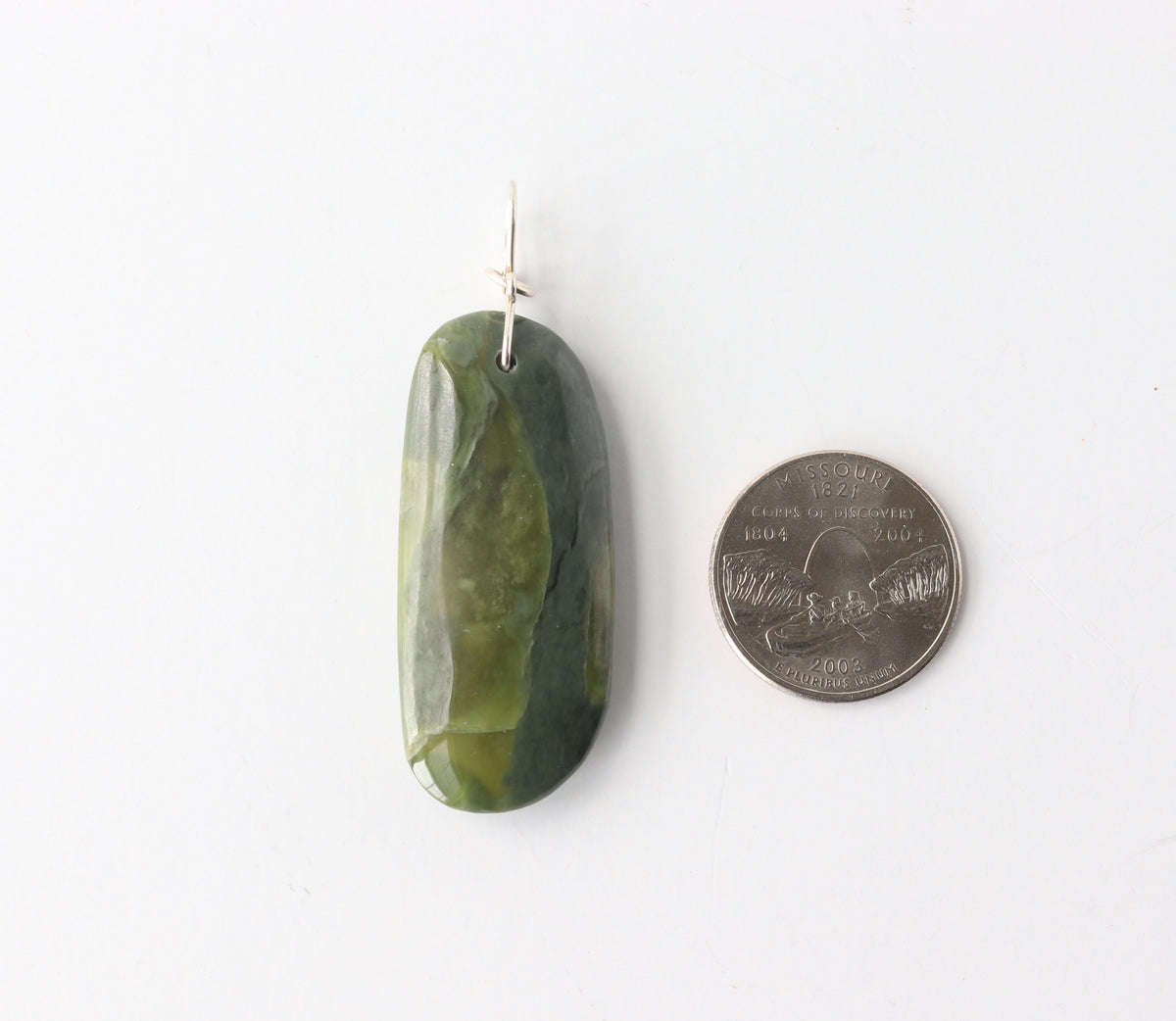 Green jade pendant next to a quarter on a white background