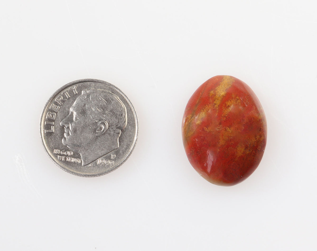A Chrysocolla Cuprite with warm reds and yellow cabochon shown next to a US dime for scale, on a plain white background.