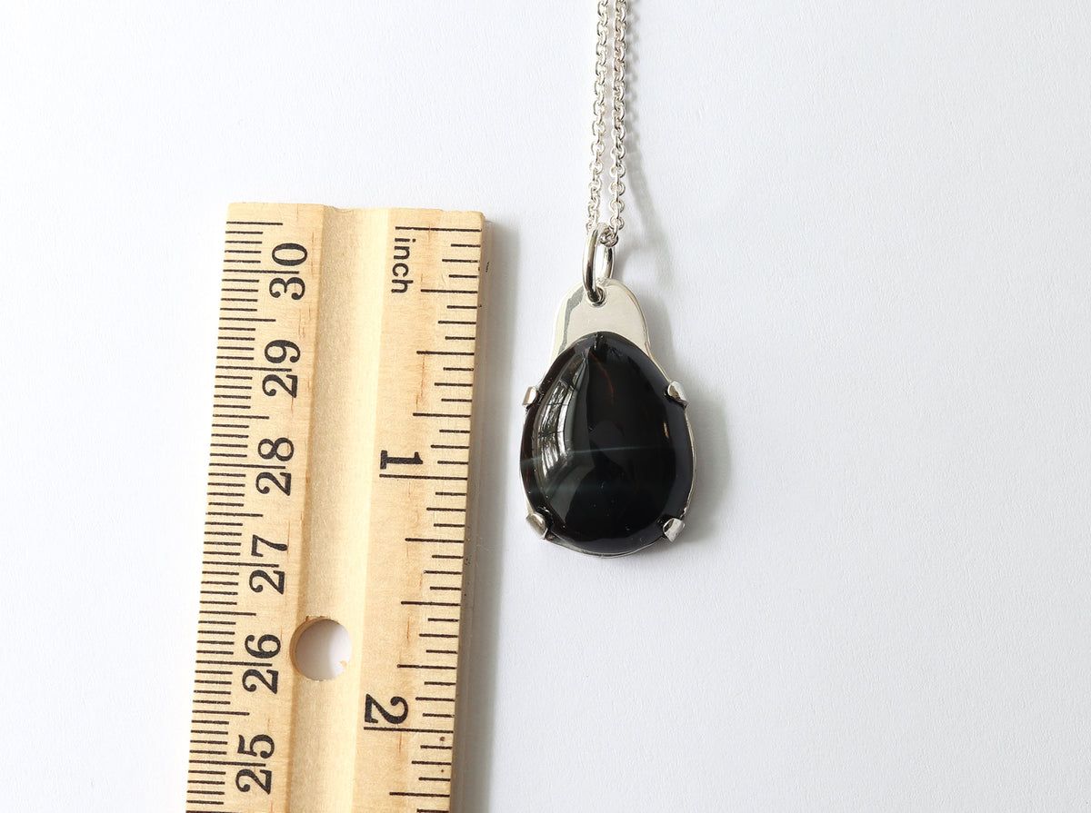 Natural Blue Tiger’s Eye pendant in Argentium 935 Silver with silver chain, shown next to a wooden ruler for scale on a white background.
