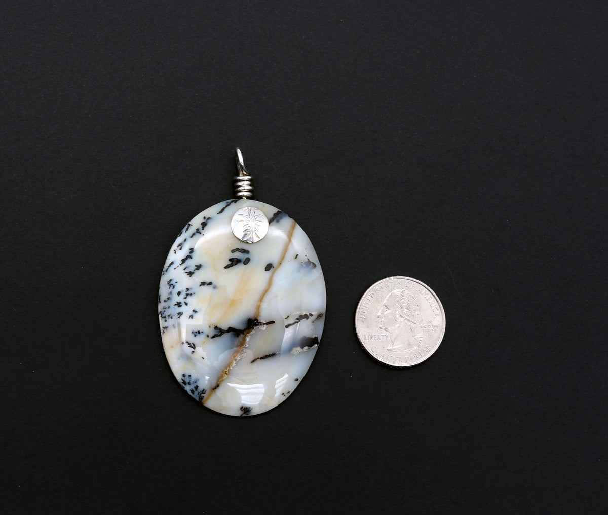 Handcrafted Dendritic Agate pendant with Argentium 935 Silver bail, 66.54mm, laid flat on a black background next to a U.S. quarter for size comparison.  
