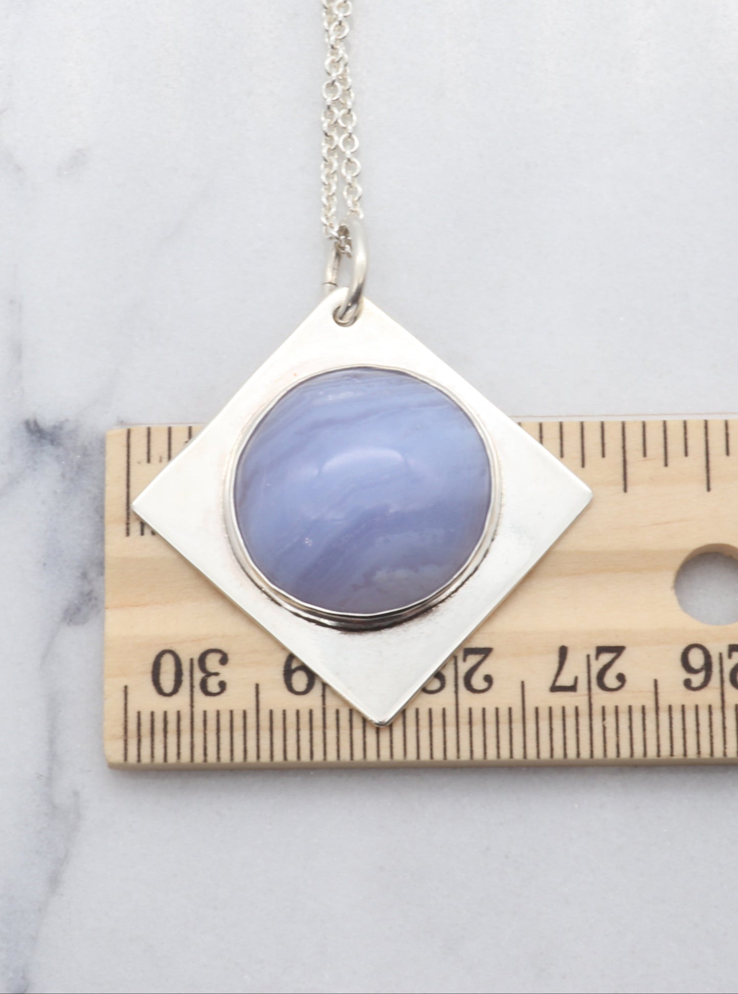 Blue Lace Agate Pendant Necklace on a marble surface next to a ruler for scale.