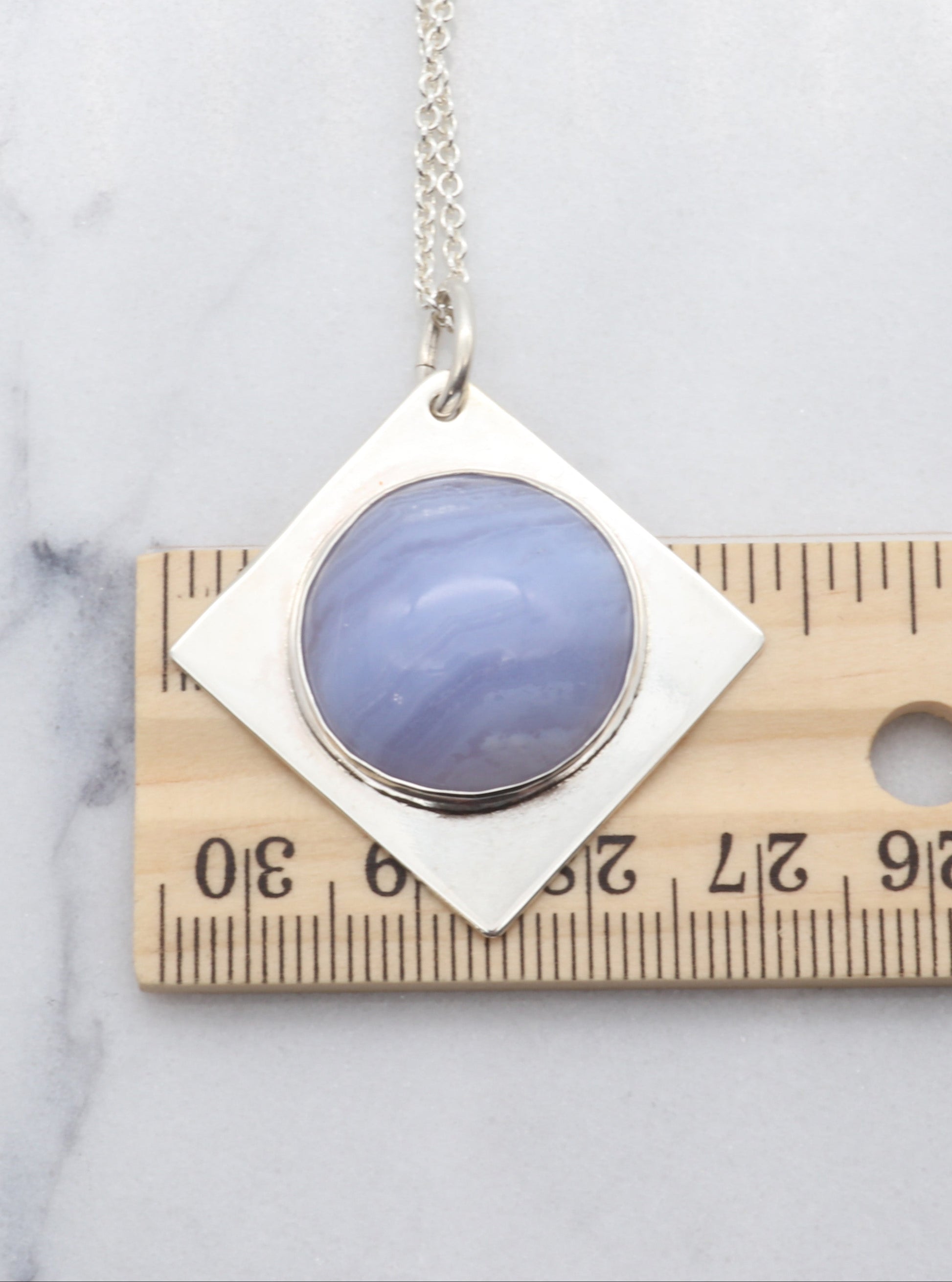 Blue Lace Agate Pendant Necklace on a marble surface next to a ruler for scale.