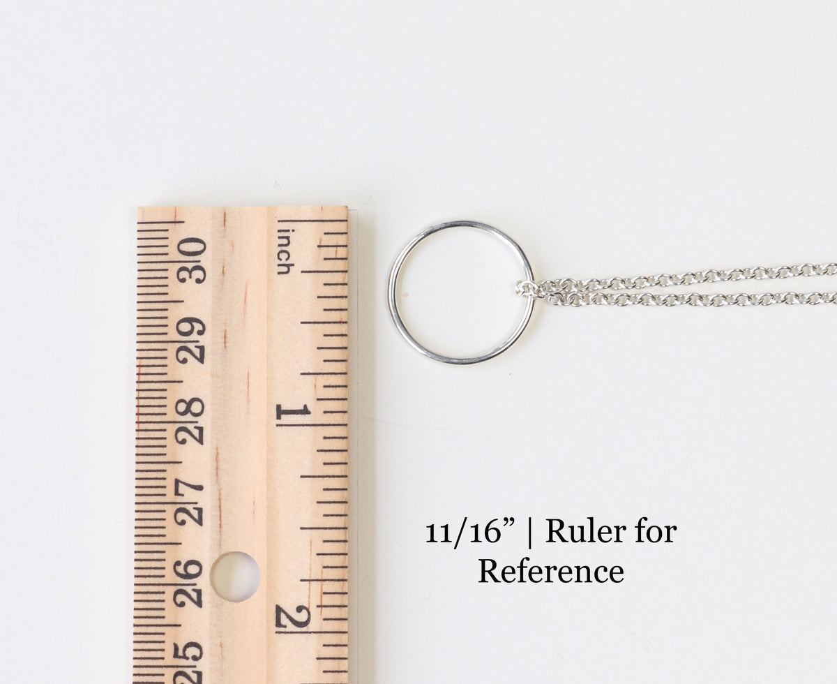 A silver chain necklace with a round ring pendant shown next to a wooden ruler for scale on a white background, with text reading '11/16" | Ruler for Reference'.