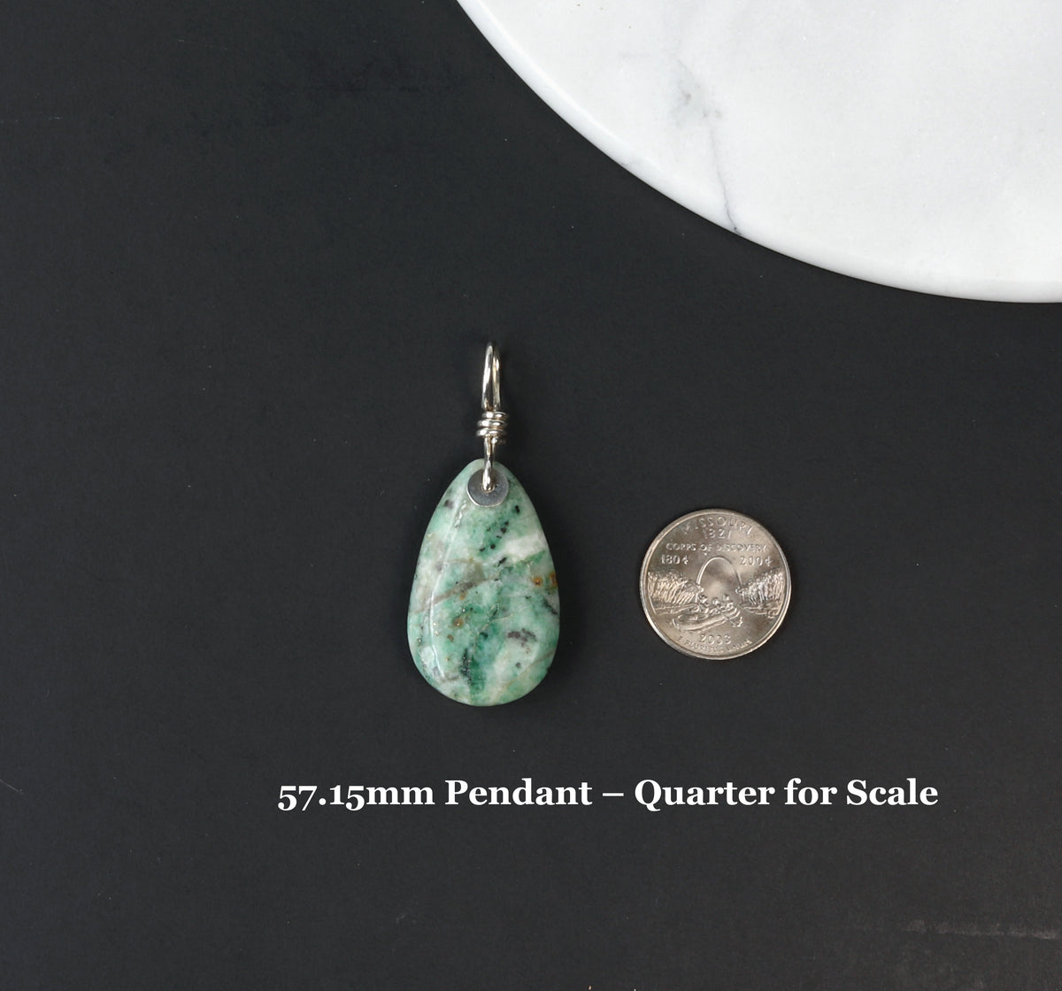African turquoise jasper Pendant shown next to quarter for scale with text overly 57.15mm Pendant Quarter for Scale. Shown on black background next to white marble slab.