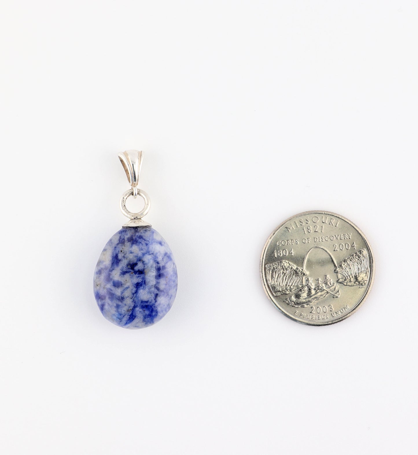 A teardrop-shaped blue sodalite with white speckles natural stone pendant with a silver bail, shown next to a U.S. quarter for scale.