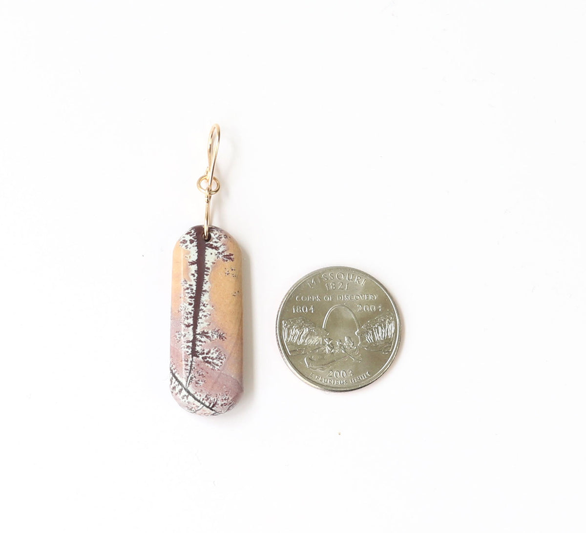 A natural Sonoran dendrite rhyolite pendant with a gold fill wire loop. The pendant is shown next to a Missouri state quarter to illustrate scale of size.