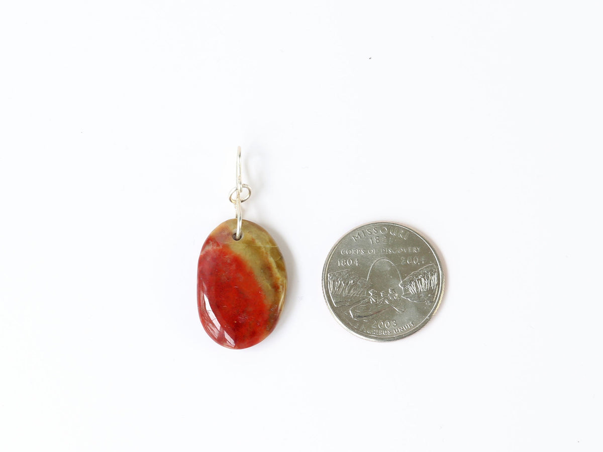 An oval Sonoran Sunrise pendant made of polished red and yellow agate with a Argentium silver loop, shown next to a US quarter for scale on a white background.