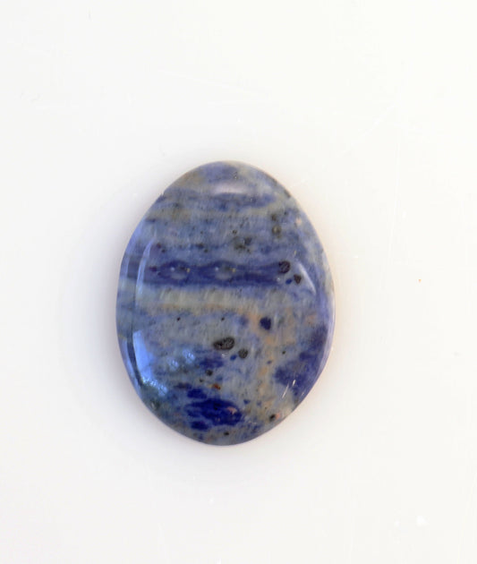 Hand-cut oval Blue Foidolite cabochon with layered deep blue, slate blue and gray natural mineral patterning on a white background.