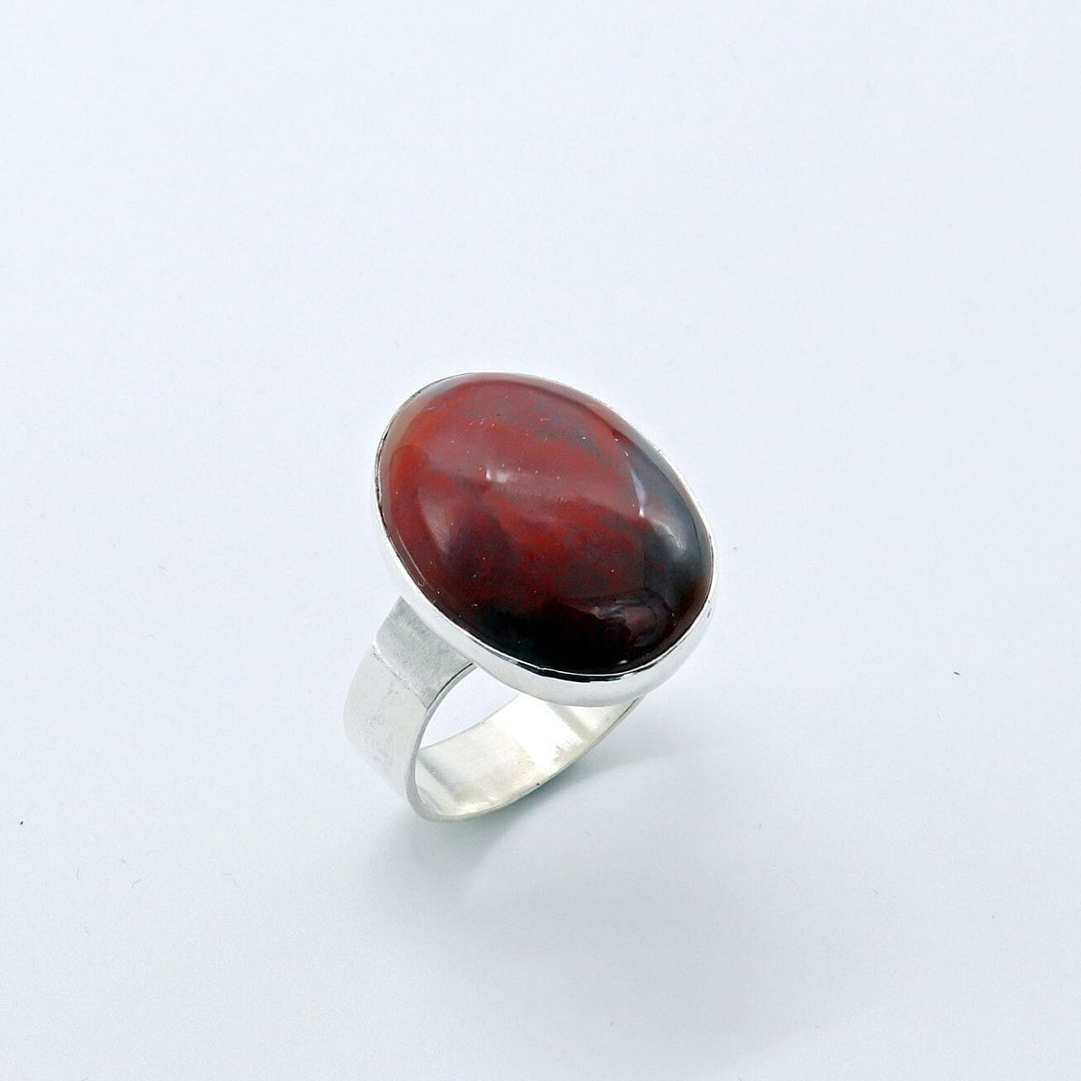 Handcrafted Petrified Rainbow Wood ring with oval red and dark brown gemstone set in polished Argentium 935 silver, three-quarter view.