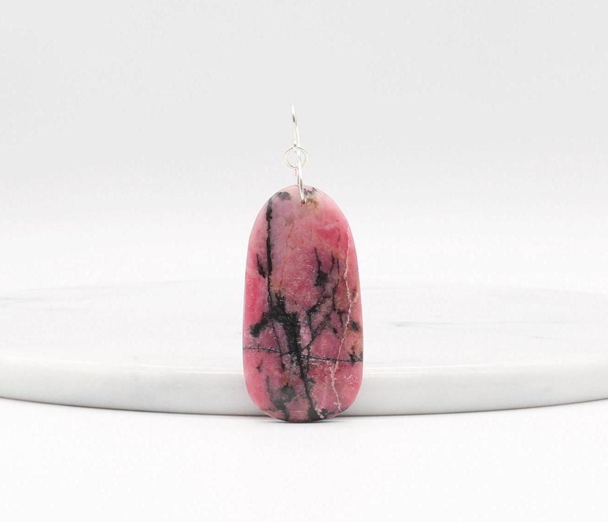 Reverse side shown of this Natural Rhodonite pendant necklace with solid Argentium 935 Silver bail and chain standing against a white marble slab and shown on light gray background.
