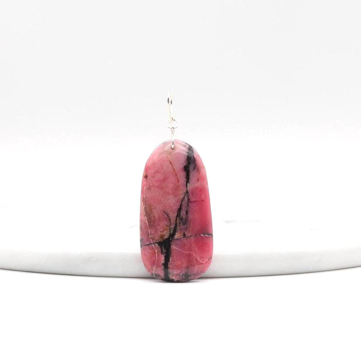 Natural Rhodonite pendant necklace with solid Argentium 935 Silver bail and chain standing against a white marble slab and shown on light gray background.