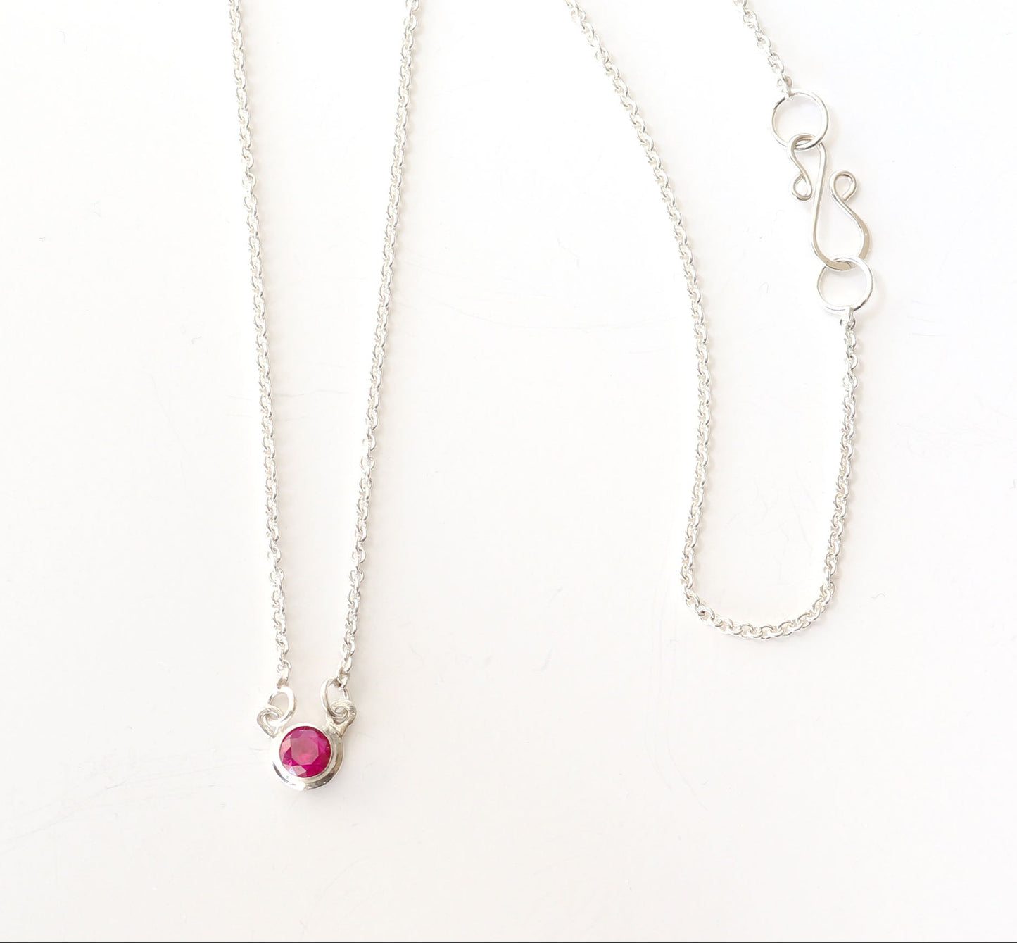 Overhead closeup of lab Ruby necklace pendant with closeup of s-hook clasp in Argentium Silver. Shown on white background.