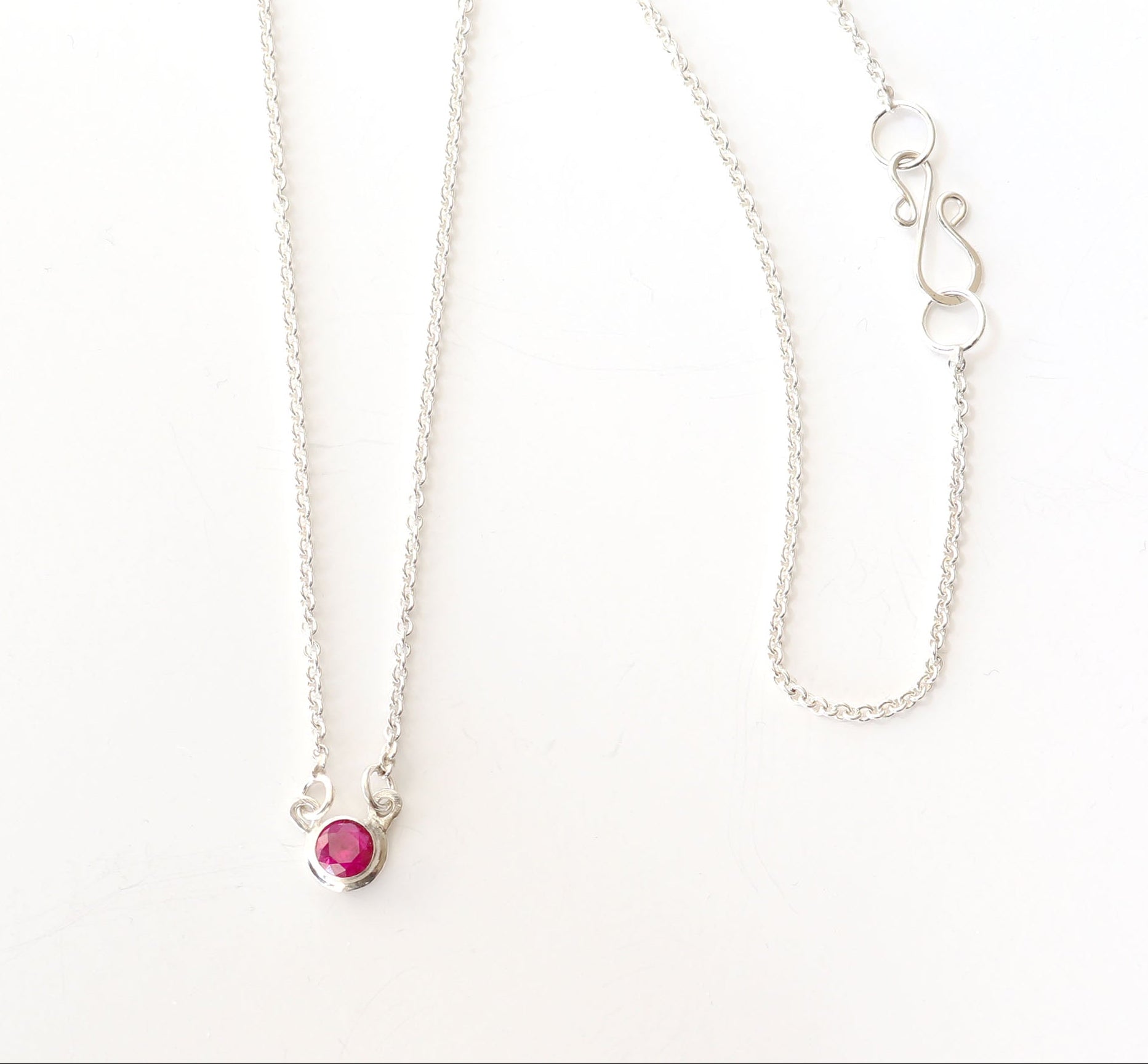 Overhead closeup of lab Ruby necklace pendant with closeup of s-hook clasp in Argentium Silver. Shown on white background.