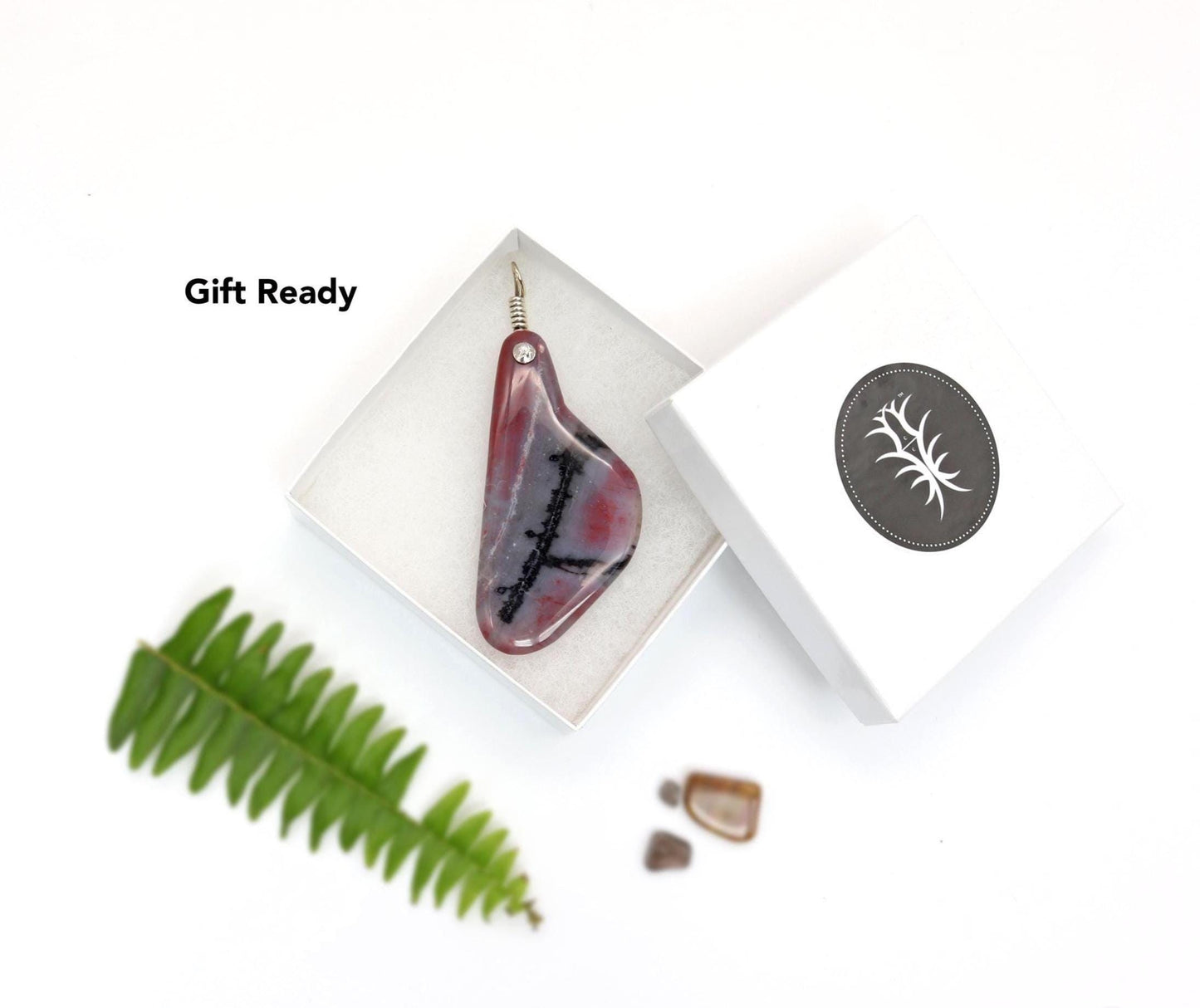 Handcrafted Arizona Petrified Rainbow Wood charm, 4 inches long, with a 935 silver bail, inside a white gift box, placed on a white background, showcasing bold red and carbon black stripes and swirls, highlighting the signature packaging