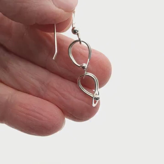 Demo clip hand holding solid Argentium handmade loop earrings against white background