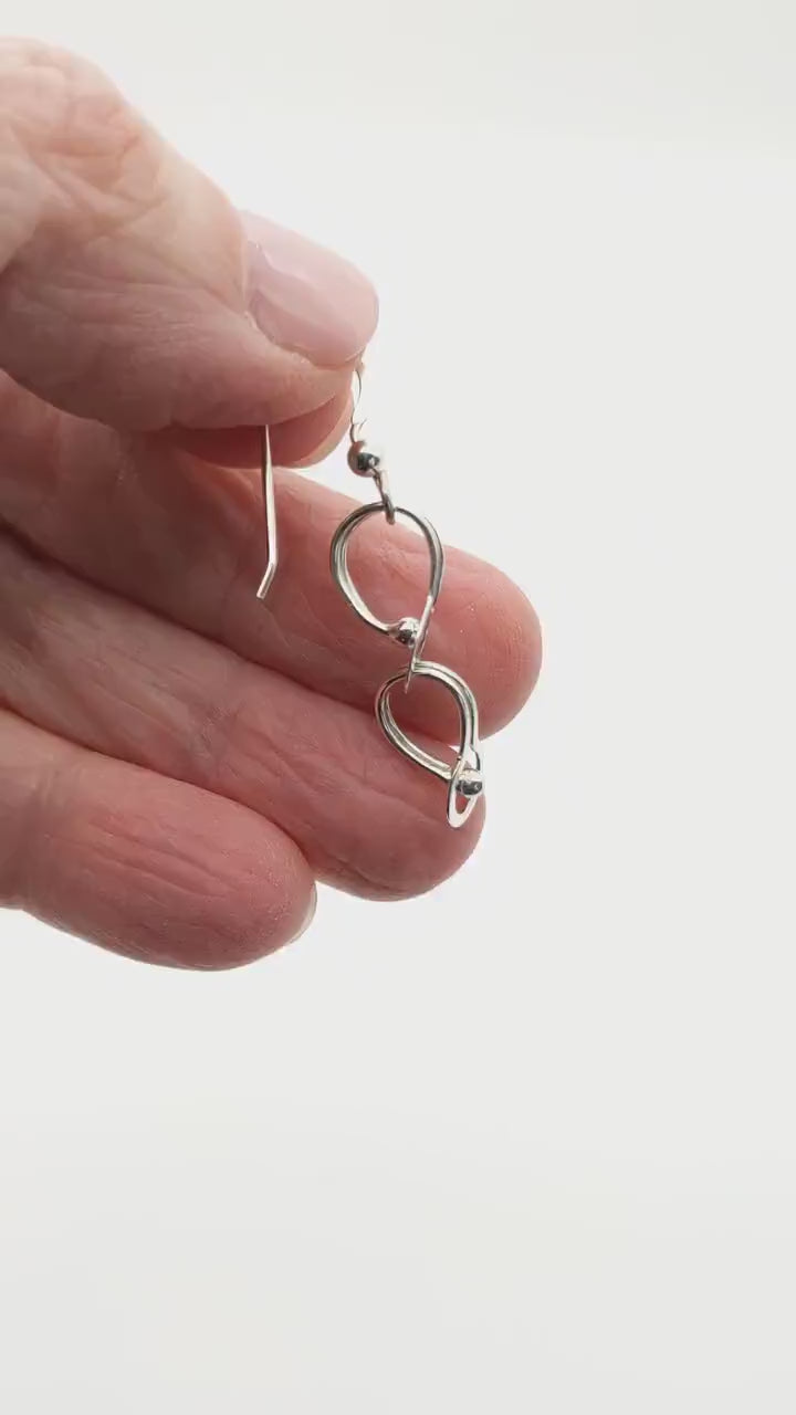 Demo clip hand holding solid Argentium handmade loop earrings against white background