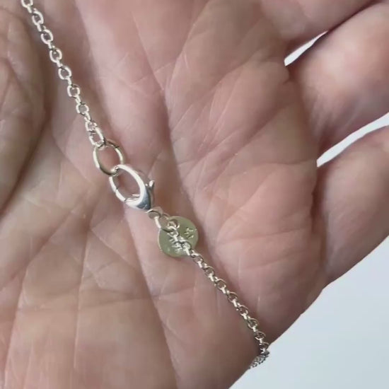 Demo clip of Argentium oval chain highlighting teardrop lobster clasp in human hand against light gray background.