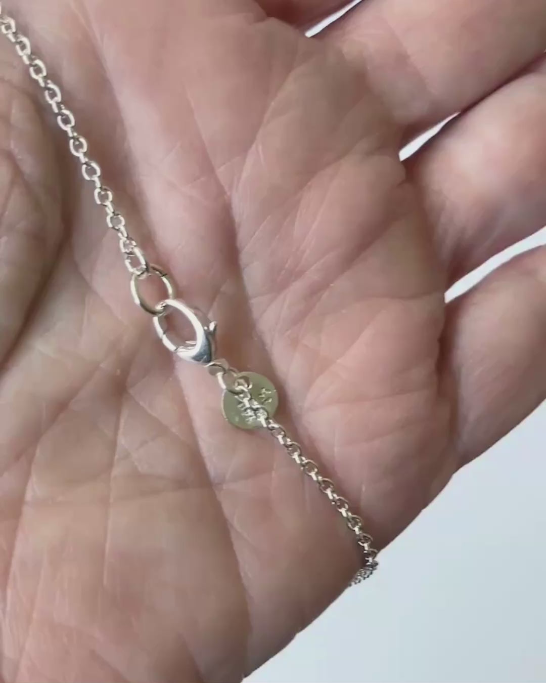 Demo clip of Argentium oval chain highlighting teardrop lobster clasp in human hand against light gray background.