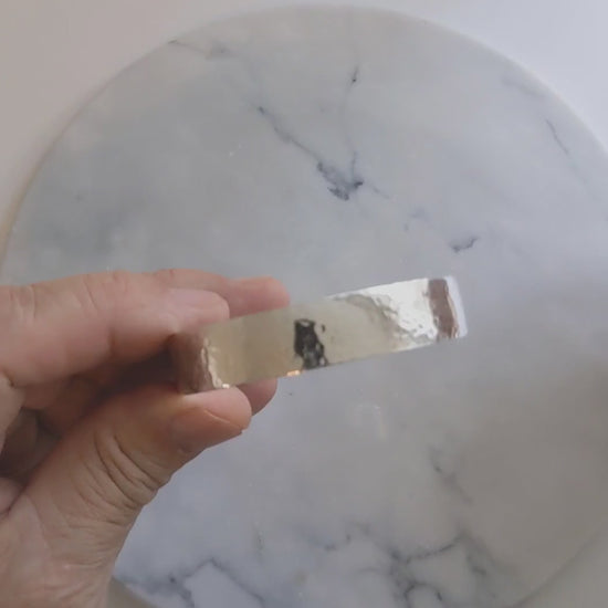 Hand-hammered sterling silver cuff bracelet with a softly curved profile, shown on a 7.5-inch wrist against a light marble-patterned background.