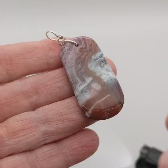 Demo clip of a Red Mexico Agate light display of the translucent features of this mauve and white  tage shaped pendant with Argentium wire loop shown against white background.