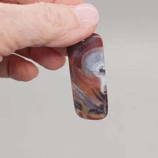 Demo of banded agate pendant features flowing bands of deep red, purple, orange, black, and white on light gray background.