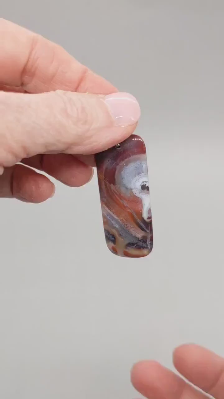 Demo of banded agate pendant features flowing bands of deep red, purple, orange, black, and white on light gray background.