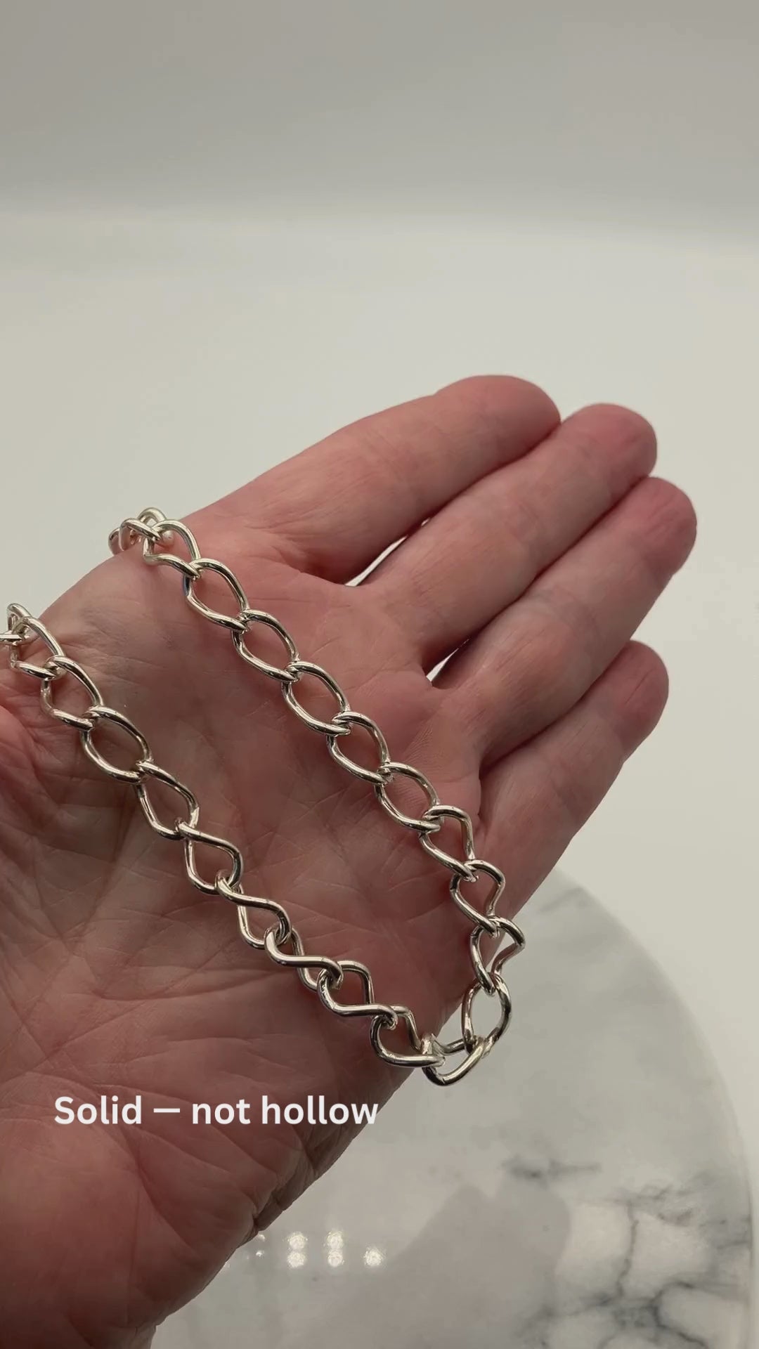 Video showing a solid Argentium® silver oval link necklace resting in a hand, demonstrating its weight and shine. On-screen text reads: “Solid — not hollow,” “45 grams Argentium® silver,” and “Made to wear every day.