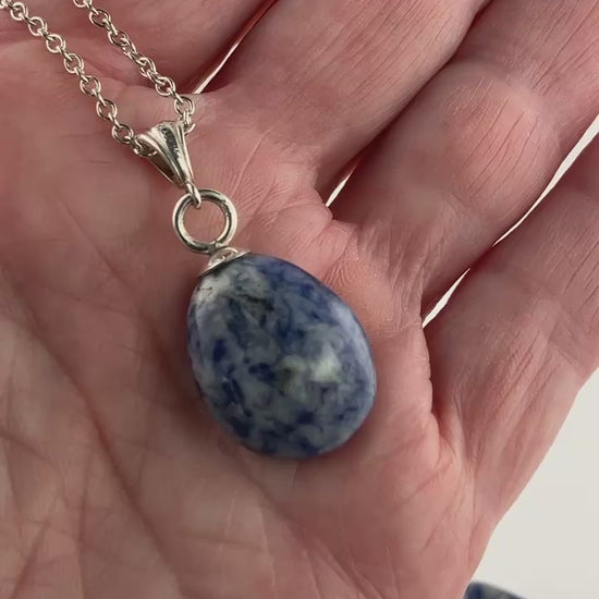 Demo clip of Blue Sodalite pendant with silver bail and necklace against background of white and a few chips of raw sodalite shown in background.