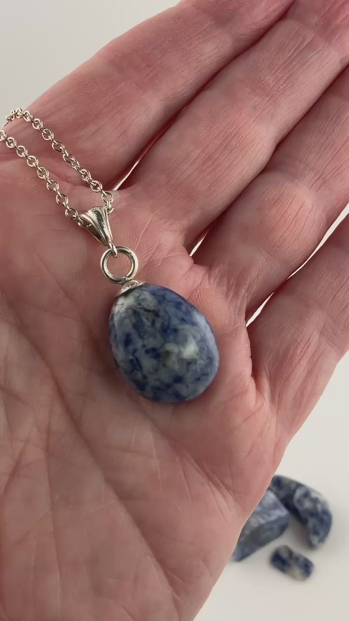 Demo clip of Blue Sodalite pendant with silver bail and necklace against background of white and a few chips of raw sodalite shown in background.