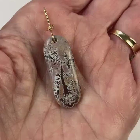 Dendritic Rhyolite Pendant with Gold-Filled Infinity Bail is shown in demo of pendant in a hand showing both sides of pendant.